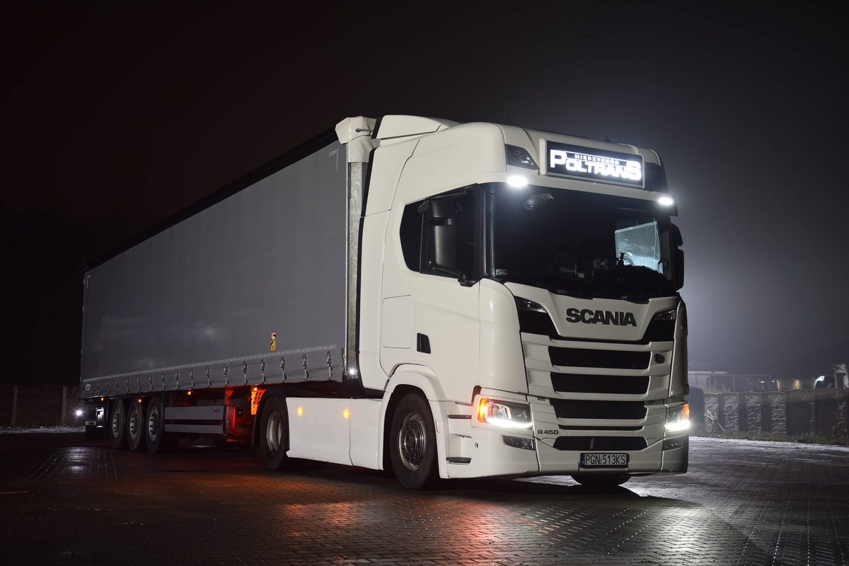 Biała Scania R 450 POLTRANS z naczepą firankową nocą na placu