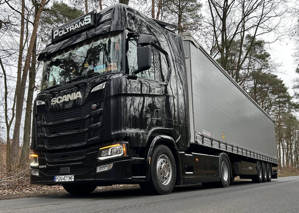 Czarna Scania 500 S POLTRANS z naczepą firankową na leśnej drodze